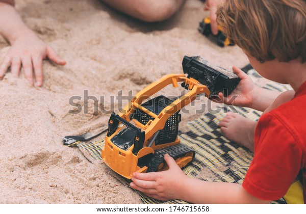 Father\'s day. Dad and son. Little son plays toys\
with dad on the beach with sand. Happy loving family. Happy family\
father and child. Toy cars. Hands of a man and a small child on the\
beach. Together