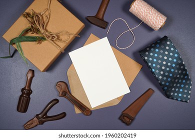 Father's Day Or Masculine Birthday Greeting Card Invitation Flatlay Styled With Gift, Chocolate Tool Set And Tie. White Product Mock Up With Negative Copy Space For Your Text Or Design Here.