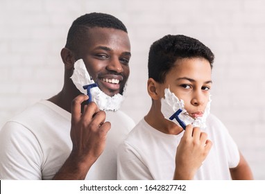 Father's Example. Teen Black Guy Shaving Together With Dad, Holding Rasor And Looking At Camera, Selective Focus