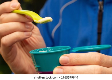 Fathers Hand Feeding Little Baby First Solid Food. Holding A Spoon With Rice Cereal Porridge And Baby Food Container