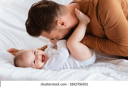 Father's Love. Dad Cuddling Bonding With Little Baby Son Spending Time Together Lying On Bed At Home. Loving Daddy Laughing Playing With Cute Toddler. Fatherhood, Parenting Joy And Child Care