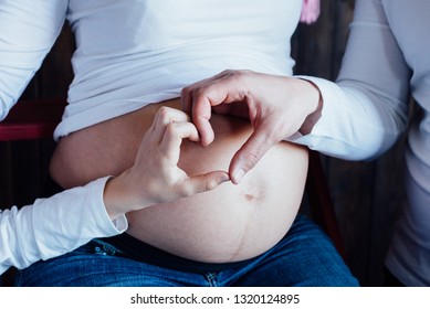 Father's And Son's Hand Creating Heart Next To Pregnant Belly Of Woman