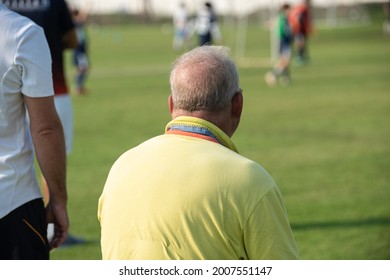 Fathers Watching Their Sons Playing Football In A School Tournament On A Sideline With A Sunny Day. Sport, Outdoor Active, Lifestyle, Happy Family And Soccer Mom And Soccer Dad Concepts.