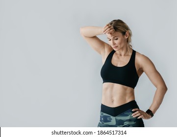 Fatigue After Morning Workout At Home During Covid-19 Quarantine. Muscular Adult Lady Athlete Or Trainer In Sportswear With Fitness Tracker Wiping Sweat From Forehead, Isolated On Gray Background