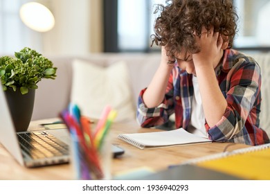 Fatigue. Portrait of tired latin boy holding his head, looking sad while sitting at the desk and doing homework at home
