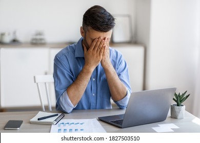 Fatigue From Work. Stressed male entrepreneur covering face with hands at workplace, tired after using laptop, having business problems, overworked businessman feeling unhappy and unwell, free space