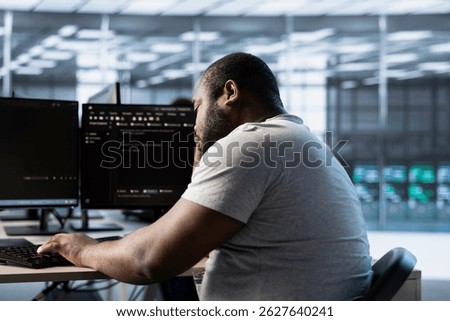 Fatigued engineer falling asleep while typing on computer in server hub, monitoring data center energy consumption. Sleepy employee struggling to stay awake while inspecting rackmounts