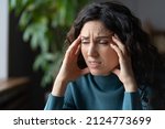 Fatigued overworked young woman suffering from migraine or tension headache at workplace, feeling throbbing or pulsing pain in head. Anxious female thinking and worrying about personal problems