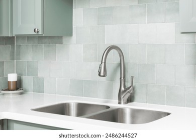 A faucet detail in a kitchen with sage green cabinets, square tile backsplash, and white marble countertop. - Powered by Shutterstock