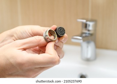 Faucet nozzle covered with scale and limestone in a male hand. The concept of low-quality running water. Selective focus on nozzle.