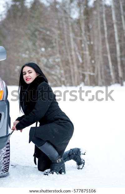 Fault car in the winter. Young\
beautiful girl trying to repair the car, engine repair, tire\
change