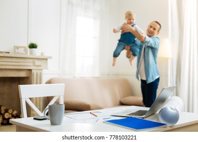 Favorite Game. Cheerful Kind Attentive Father Having Fun With His Cute Little Baby After Coming Home From Work And Leaving All The Important Tasks On The Table