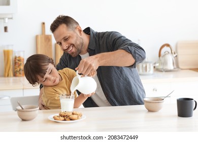 Favorite morning drink. Happy little boy helping his father to pour fresh milk into glass, enjoying healthy breakfast at home kitchen, free space - Powered by Shutterstock