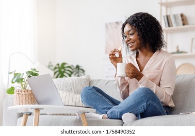 Favorite Pastime. Young Black Girl Relaxing At Home With Laptop And Tea, Watching Movies And Eating Crispy Waffles, Side View With Copy Space