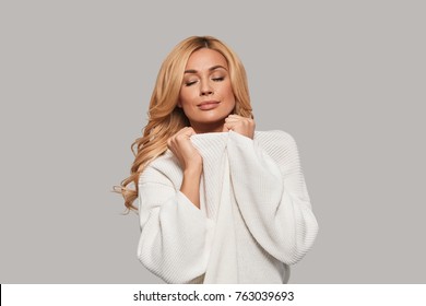 Favorite Sweater. Attractive Young Woman Touching Her Sweater And Keeping Eyes Closed While Standing Against Grey Background