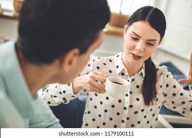 Favourite Drink. Nice Young Woman Holding A Cup Of Coffee While Talking To Her Colleague