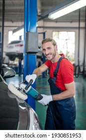 Favourite Hobby. Happy Young Adult Man Polishing Car Working In Auto Repair Shop In Good Mood