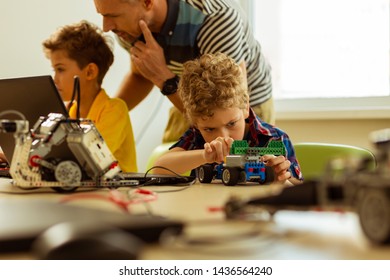 Favourite Hobby. Nice Young Boy Sitting At The Desk While Playing With A Car That He Constructed