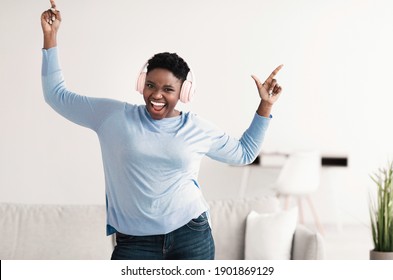 Favourite Playlist Concept. Excited Large Build African American Woman In Pink Wireless Headset Listening To Music, Dancing, Resting At Home And Looking At Camera. Young Black Chubby Female Having Fun