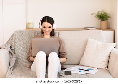 Favourite Song. Cheerful freelancer working on laptop sitting on couch and listening to music in headphones, copyspace - Powered by Shutterstock