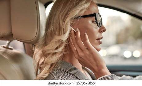 Favourite Song. Portrait Of Attractive Woman In Eyeglasses Adjusting Headphones While Driving A Car