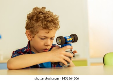 Favourite Toy. Pleasant Intelligent Boy Sitting At The Table While Playing With A Toy Car