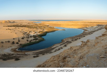 FAYOUM, EGYPT: A panoramic high-angle view of the Magic Lake surrounded by sand dunes and desert landscapes in Wadi El Rayan
