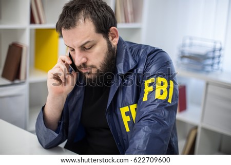 FBI agent working in his office talks on mobile phone