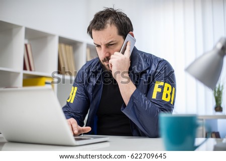 FBI agent working in his office talks on mobile and looking at laptop
