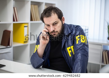 FBI agent working in his office talks on mobile phone