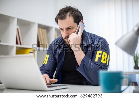 FBI agent working in his office talks on mobile and using laptop