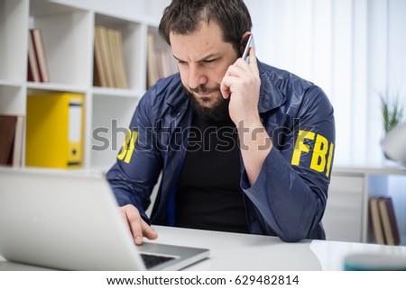 FBI agent working in his office talks on mobile an looking at laptop