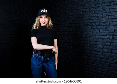 FBI Female Agent In Cap And With Gun At Studio Against Dark Brick Wall.