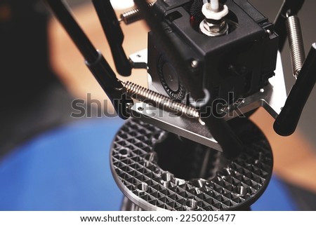 FDM-3D-printer based on delta kinematics prints a complex flange part from silver grey material. view from above on print head and infill structure. modern additive manufacturing concept