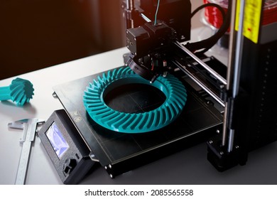 FDM-printer manufacuring turquoise bevel gear prototype from plastic filament in bright light - selective focus