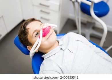 Fear of the dentist! A little boy sits in a dentist's office wearing a nasal mask to breathe nitrous oxide to relax. Concept of feeling relaxed with laughing gas. - Powered by Shutterstock