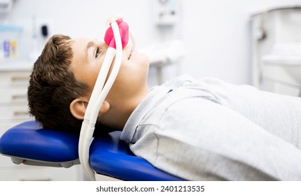 Fear of the dentist! A little boy sits in a dentist's office wearing a nasal mask breathing nitrous oxide to relax.Concept of feeling relaxed with laughing gas.Anxiety about visiting a dentist. - Powered by Shutterstock