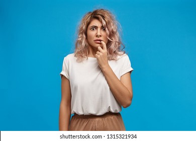 Fear, frustration and fright. Funny European girl in her twenties opening eyes wide and biting nails having scared worried look, being nervous about going to dentist. Cute female watching scary movie