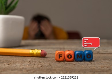 Fear of missing out concept: die composing the text fomo (fear of missing out) and a guy with hands on his head on the background