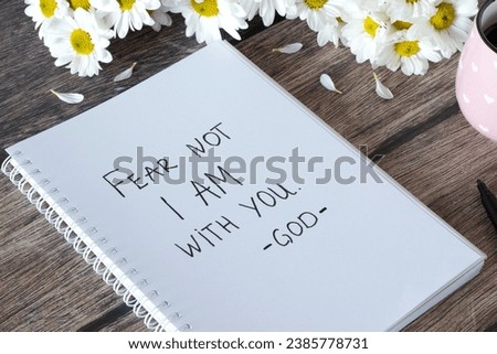 Fear not I am with you, God. Handwritten text in notebook with flowers and cup of coffee on wooden table. Inspiring bible verse. Christian concept of comfort, peace, and love of Jesus Christ.