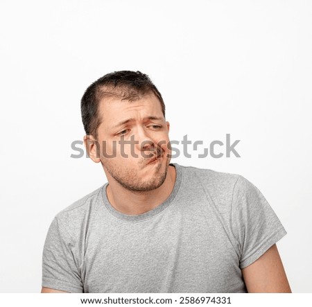 Fear of responsibility.Doubting men with skeptical expression on face isolated on white background.  An unshaven, dissatisfied men with stubble in a grey T-shirt.