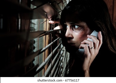 Fearful battered woman peeking through the blinds to see if her husband is home while calling for help
