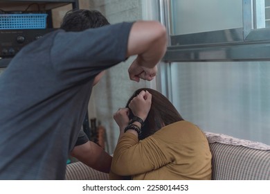 A fearful woman covers her face to protect herself from a abusive husband beating her up with his fists. Example of domestic abuse and physical violence in couples. - Shutterstock ID 2258014453