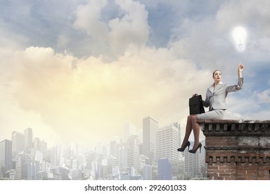 Fearless businesswoman with suitcase sitting on building top