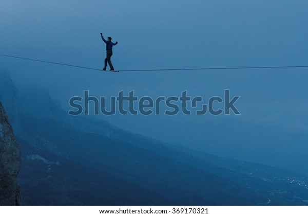 Fearless highliner walking on tight rope. At\
the height of mountains in the\
background