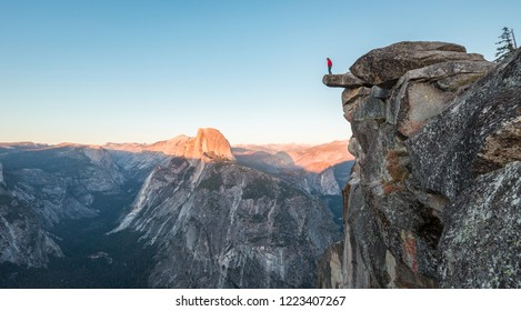 A fearless hiker is standing on an overhanging rock enjoying the view towards famous Half Dome at Glacier Point overlook in beautiful evening twilight, Yosemite National Park, California, USA - Powered by Shutterstock