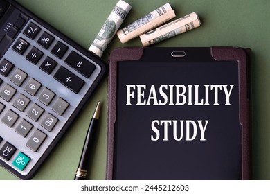 FEASIBILITY STUDY - words in an electronic notebook on the background of a calculator and banknotes