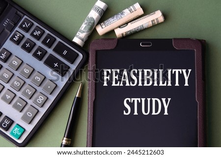 FEASIBILITY STUDY - words in an electronic notebook on the background of a calculator and banknotes