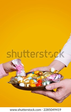Feast concept idea, woman holding sweets feast concept idea. Yellow studio background, copy space. Girl hand taking wrapped luxury chocolate. Traditional Turkish ramadan or Ramazan sweet sugar candy.