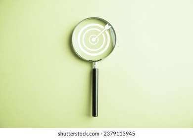Features a target board captured inside a magnifier glass, illustrating the focus on business objectives, target search concept, and attaining success. Isolated on a background with copy space.